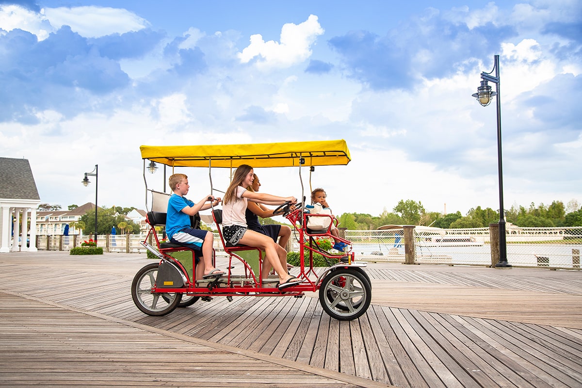 Young happy family riding a double surrey tandem bicycle on a large ocean boardwalk Outdoor summer fun with kids