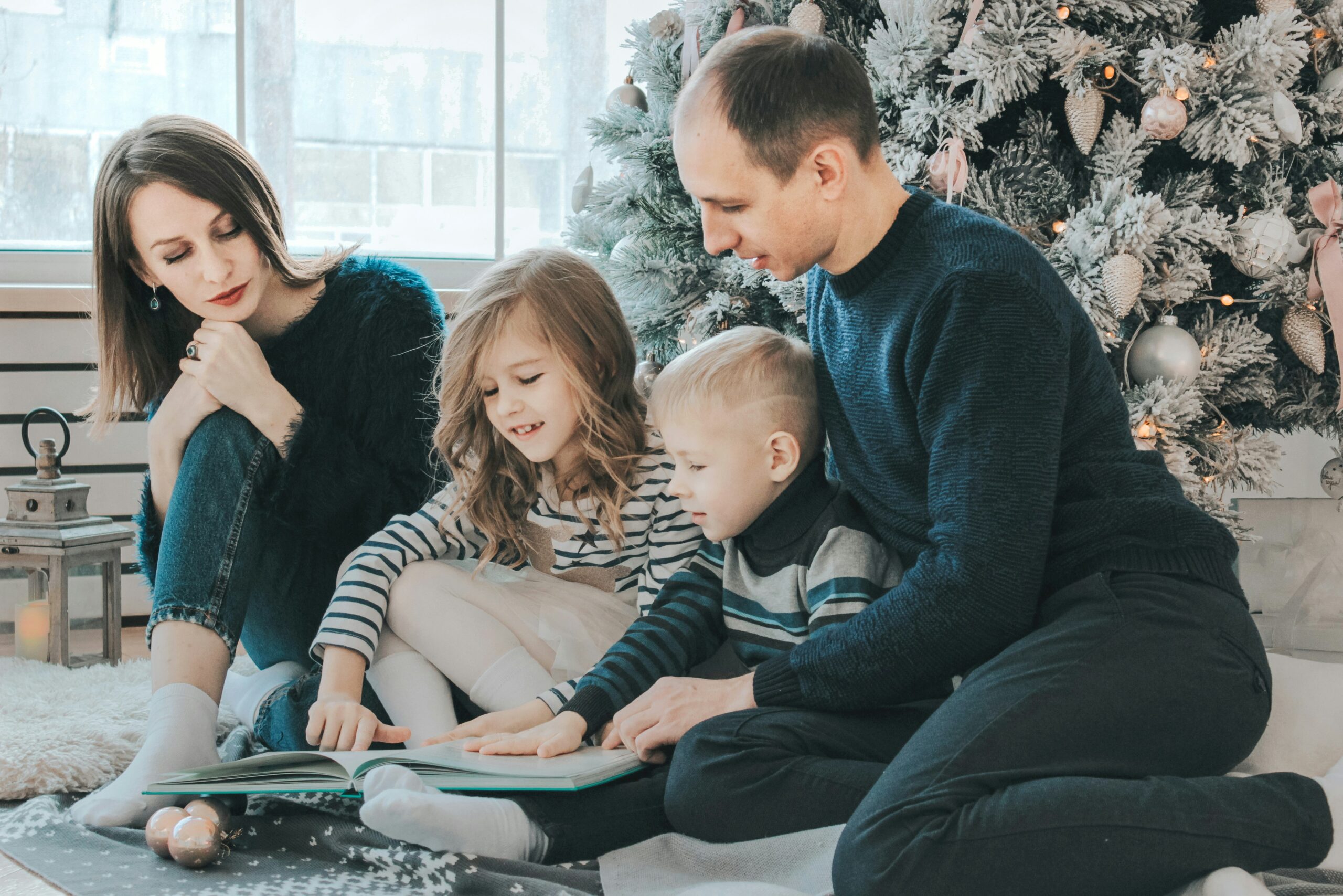 Family reading together by a Christmas tree, emphasizing togetherness and family bonding during the holiday season.