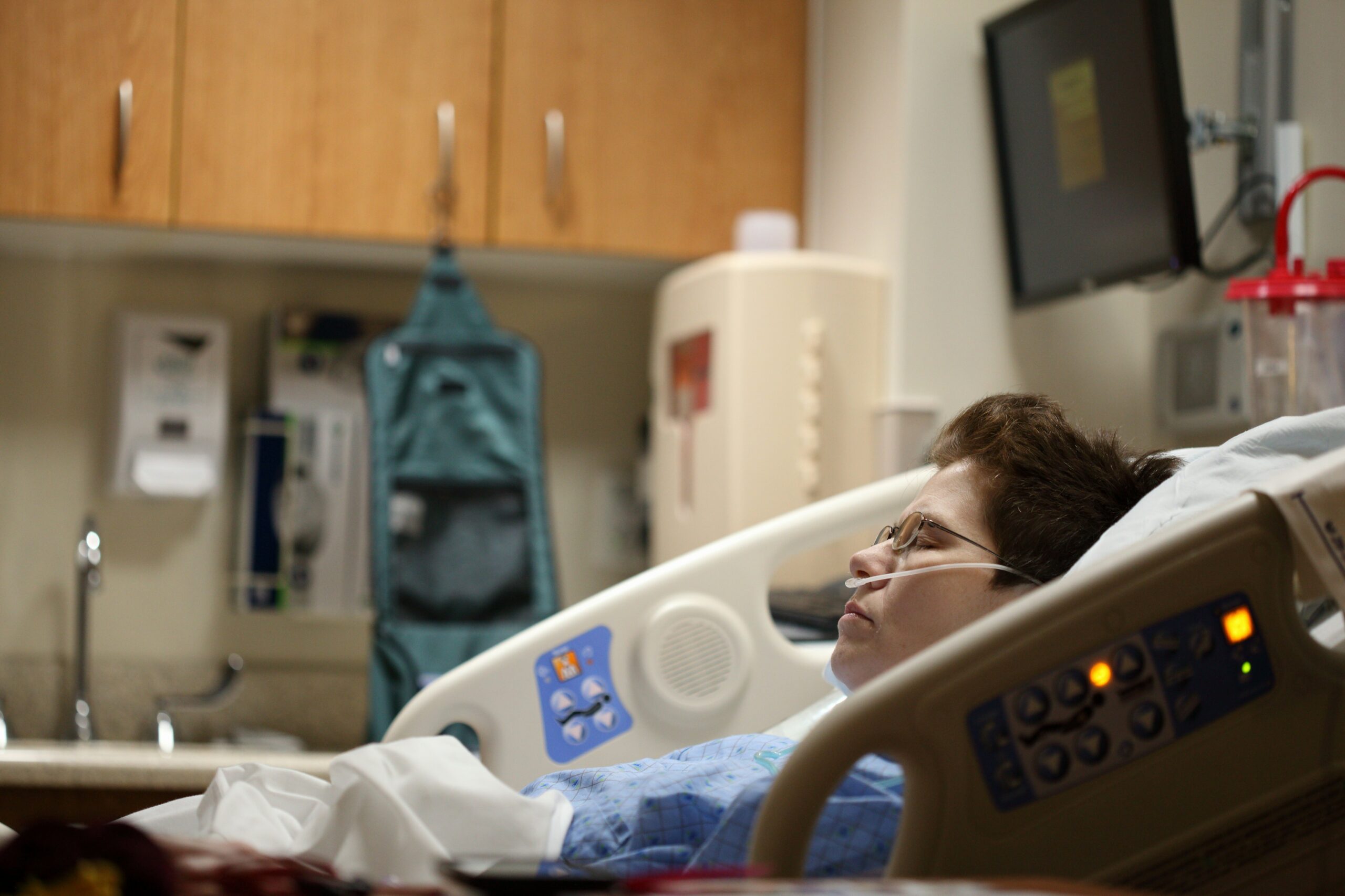 Patient in hospital bed wearing blue gown, receiving oxygen, with medical equipment in background, illustrating health conditions affecting insurance costs.