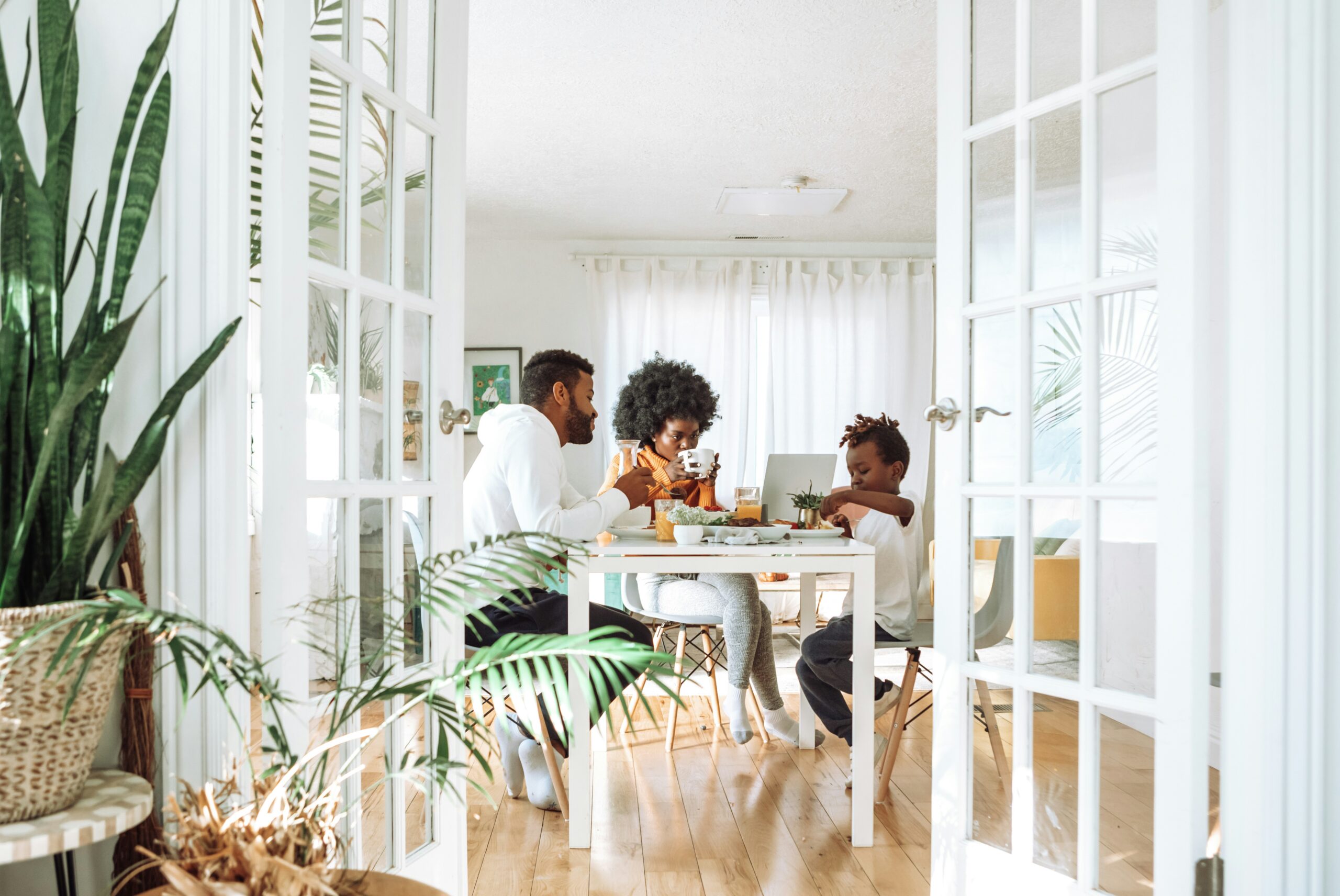A Florida family reviewing household finances at home, illustrating how subsidies and financial assistance can help make health insurance more affordable. | ProCare Consulting Family enjoying a meal together at a bright dining table, discussing healthcare options, with plants in a modern home setting.