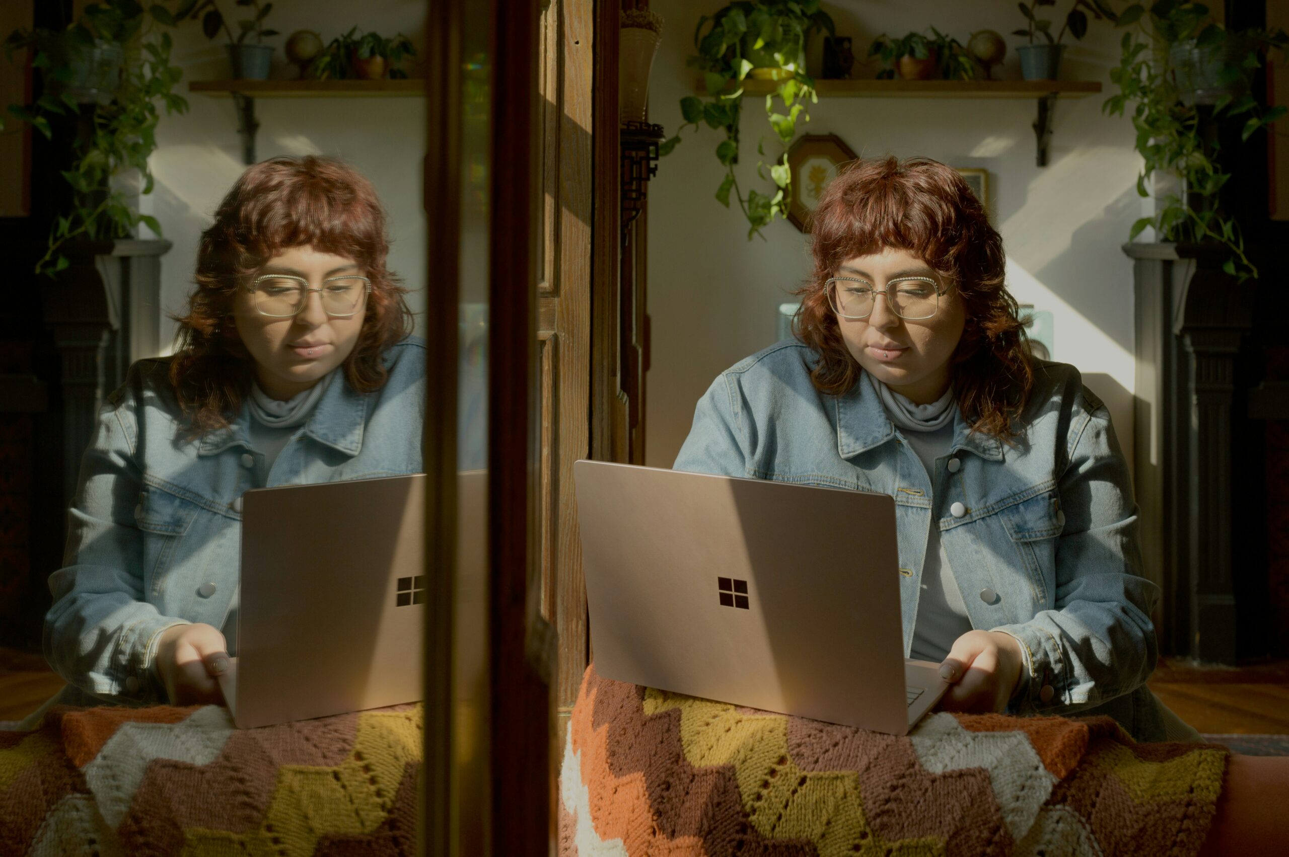 Person with curly hair and glasses sitting by a window, focused on a laptop, illustrating the importance of preparation for Medicare enrollment and planning services for Florida seniors.