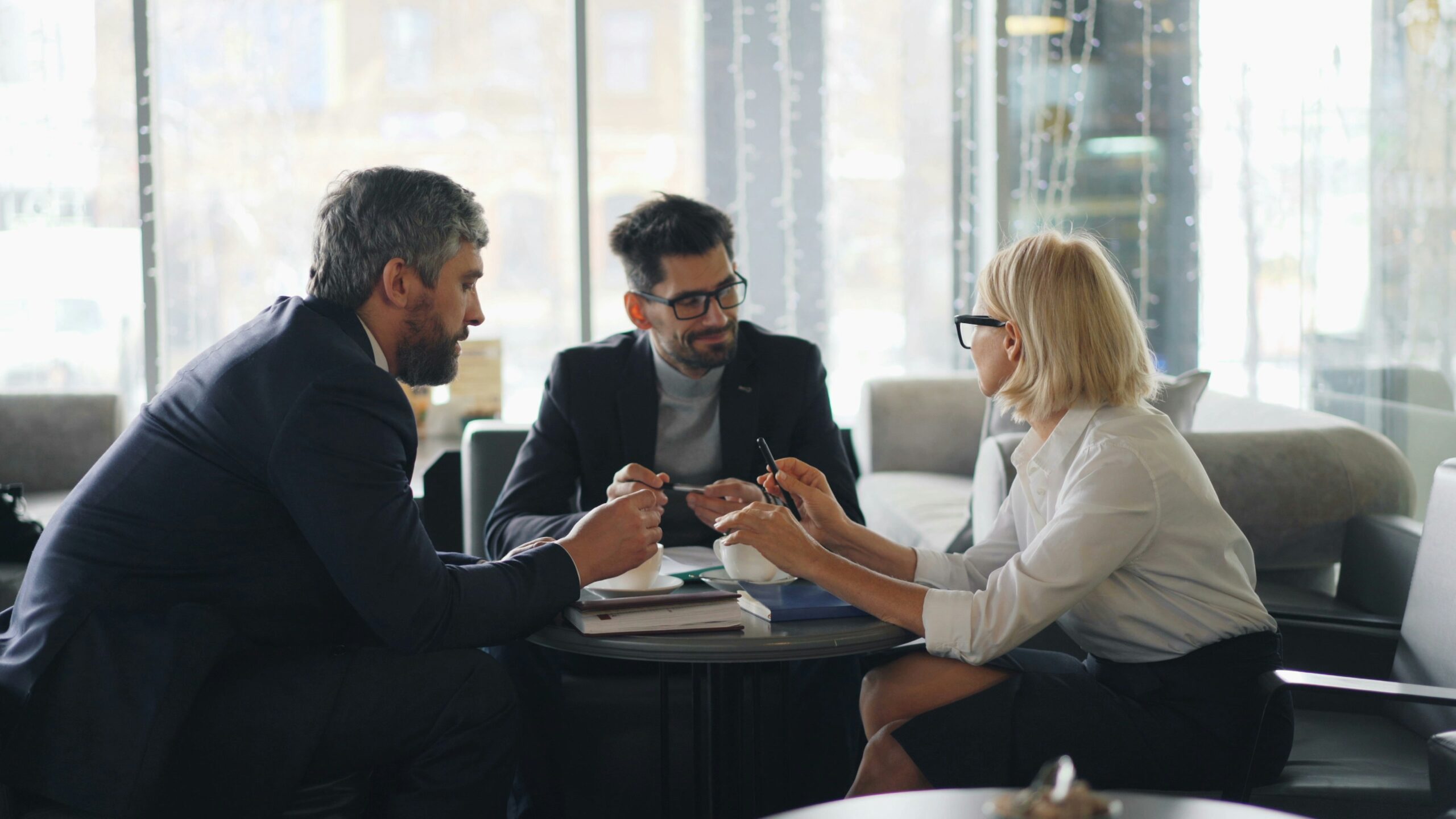 Business meeting with three professionals discussing family health insurance options, holding pens and documents, in a modern office setting.
