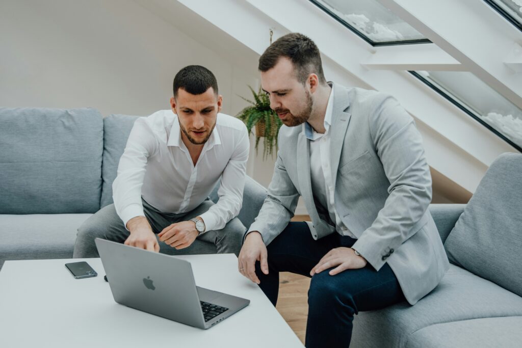 Two men discussing health insurance options while reviewing information on a laptop in a modern office setting.