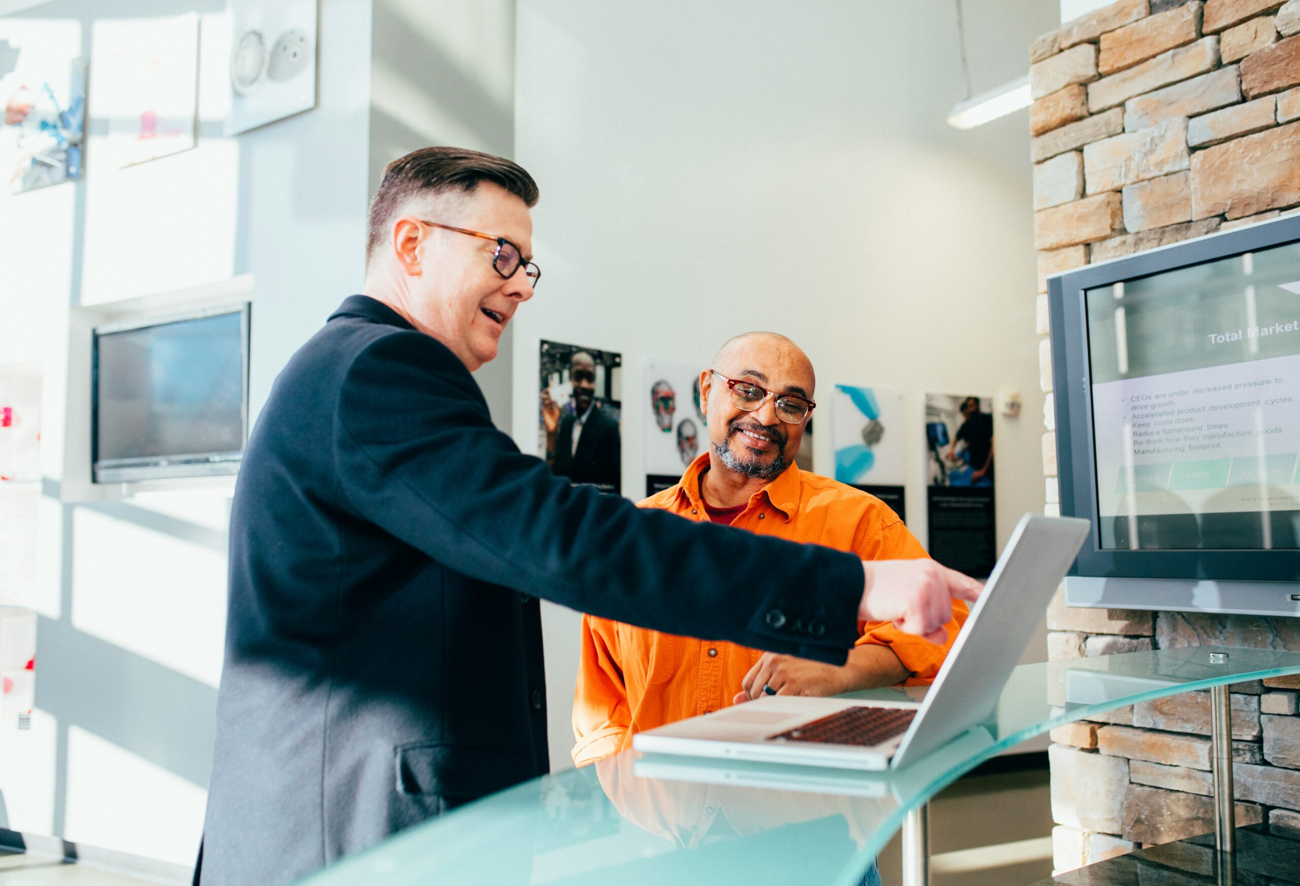 Business professionals discussing healthcare options at a reception desk, with a laptop displaying relevant information, in a modern office environment.