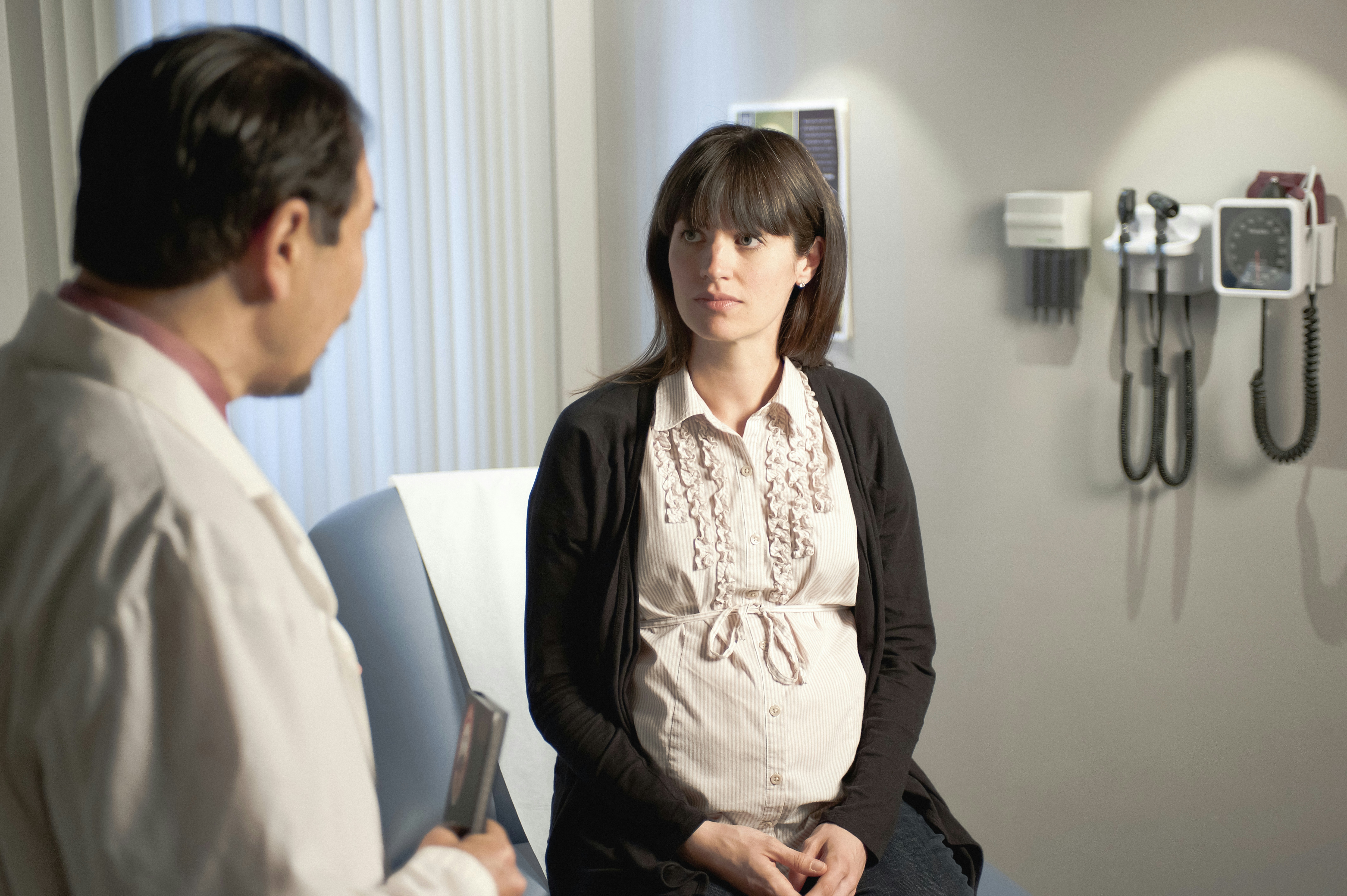 Pregnant woman consulting with a doctor in a medical office, discussing family health insurance options and prenatal care.