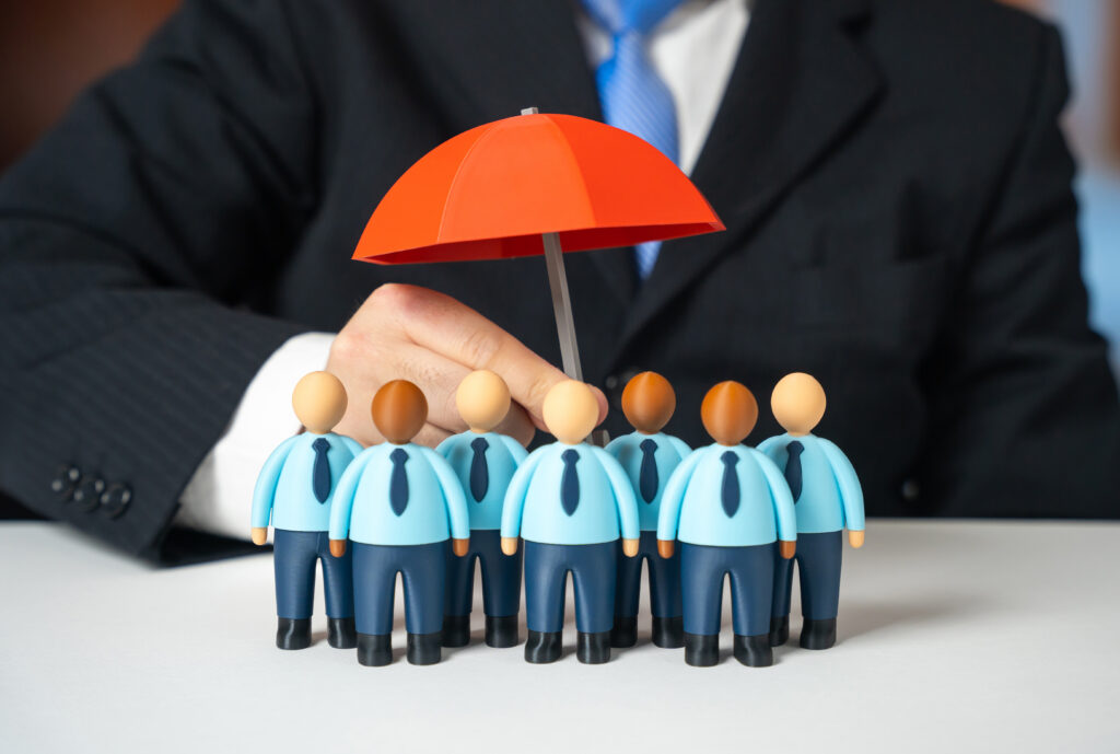 Business leader shielding employees with an umbrella symbolizing custom health insurance options designed to protect a company’s workforce.