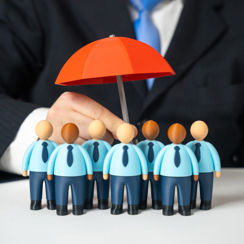 Business leader shielding employees with an umbrella symbolizing custom health insurance options designed to protect a company&rsquo;s workforce.
