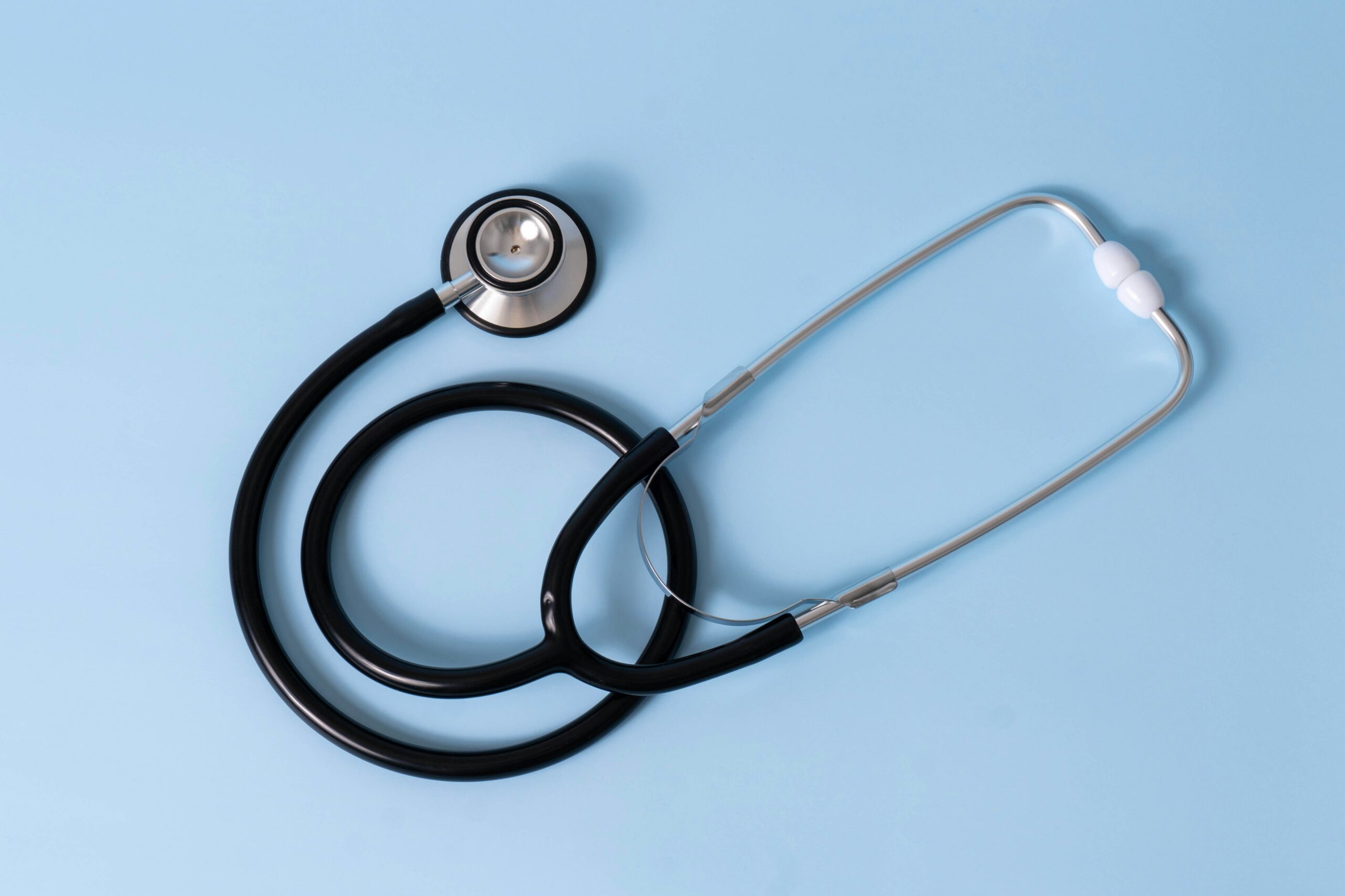 Stethoscope with metal chest piece and black tubing on a light blue background, coiled loosely on a medical-themed surface